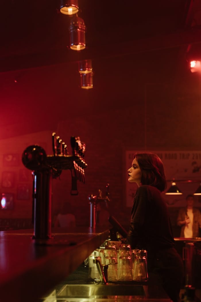 Atmospheric bar setting with a bartender next to beer taps under red lighting.