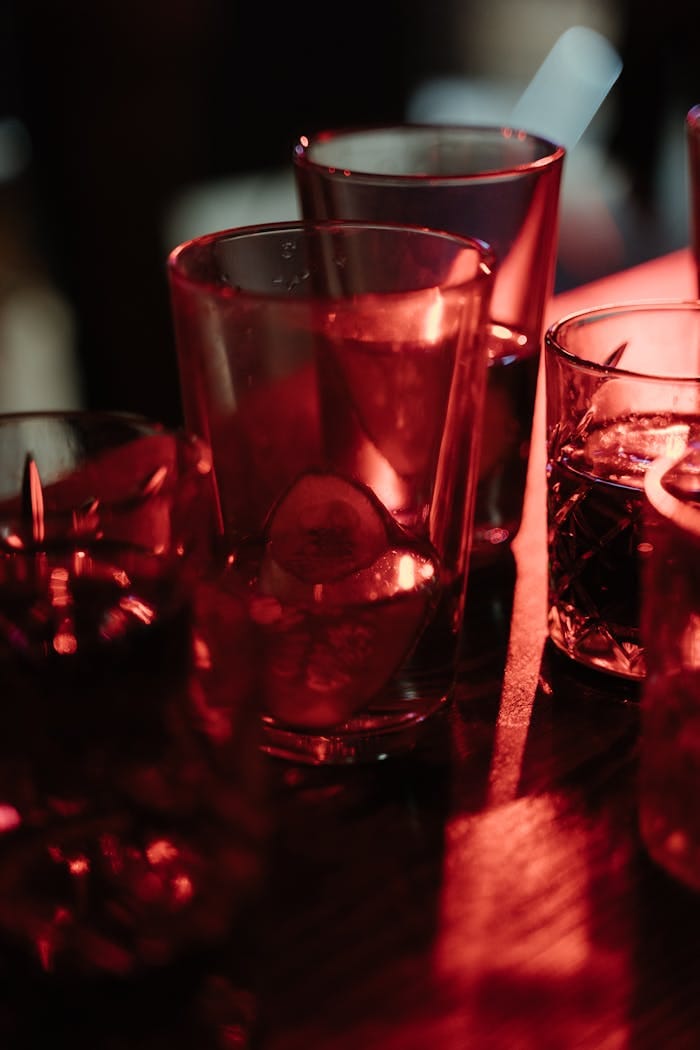 Close-up of cocktail glasses on a bar counter lit with warm red lighting.